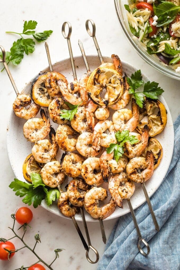 Plate holding grilled Greek shrimp on skewers.