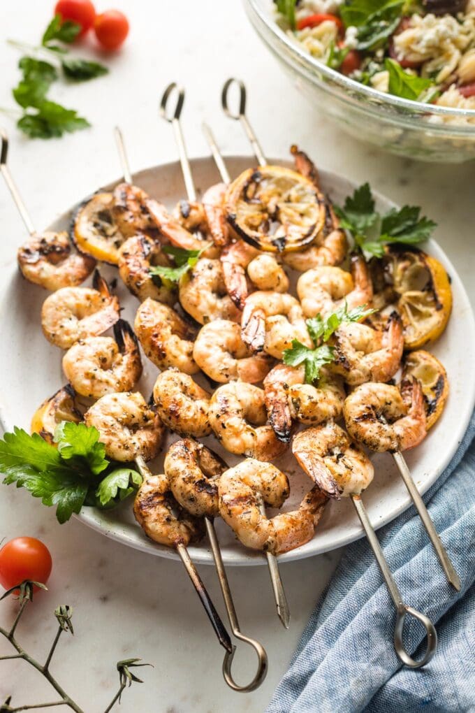 Plate holding grilled Greek shrimp on skewers.