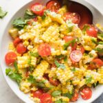 Roasted corn and tomato salad in a white bowl.