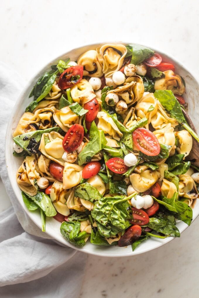 Large serving bowl full of tortellini Caprese salad with fresh mozzarella and spinach.