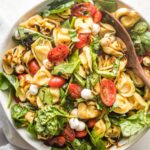 Large serving bowl full of tortellini Caprese salad with fresh mozzarella and spinach.