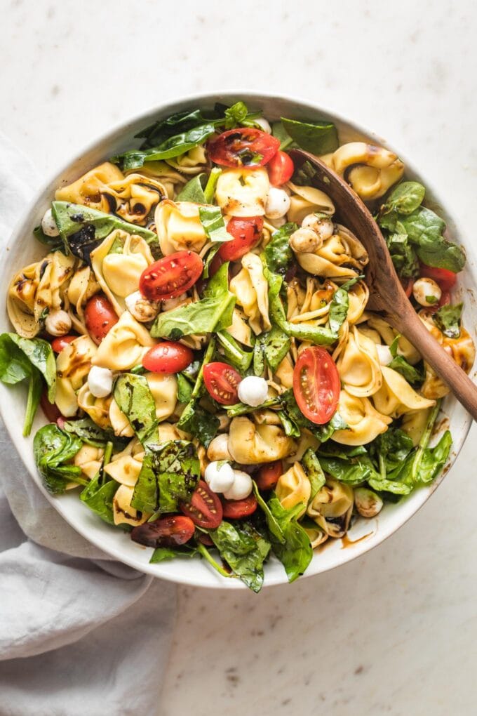 Large serving bowl full of tortellini Caprese salad with fresh mozzarella and spinach.