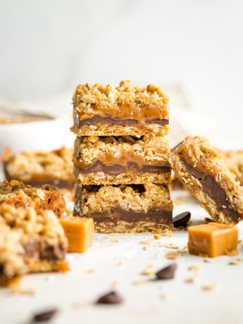 Stack of thick, chewy carmelita cookie bars, surrounded by extra chocolate chips and caramels.