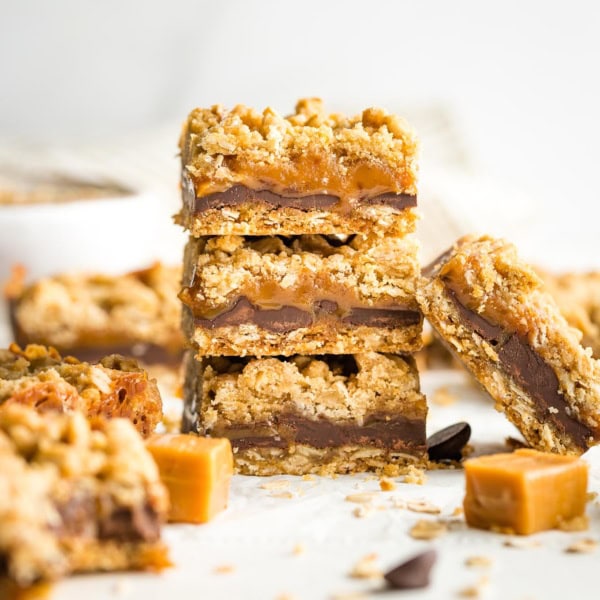 Stack of thick, chewy carmelita cookie bars, surrounded by extra chocolate chips and caramels.