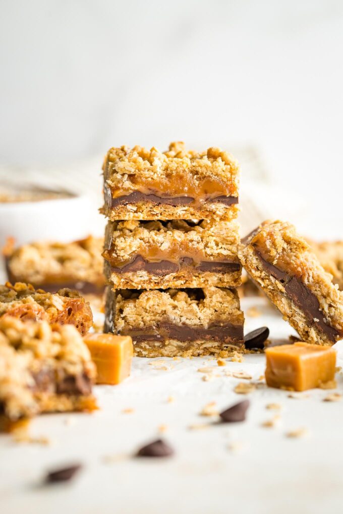 Stack of thick, chewy carmelita cookie bars, surrounded by extra chocolate chips and caramels.