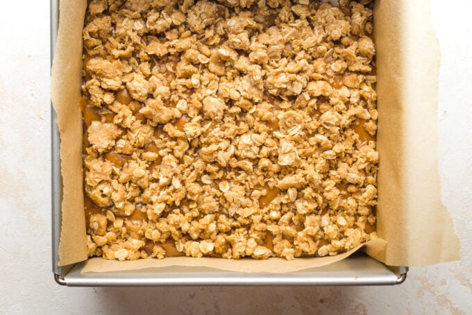 Baked bars with remaining oat cookie crust scattered on top of caramel layer.