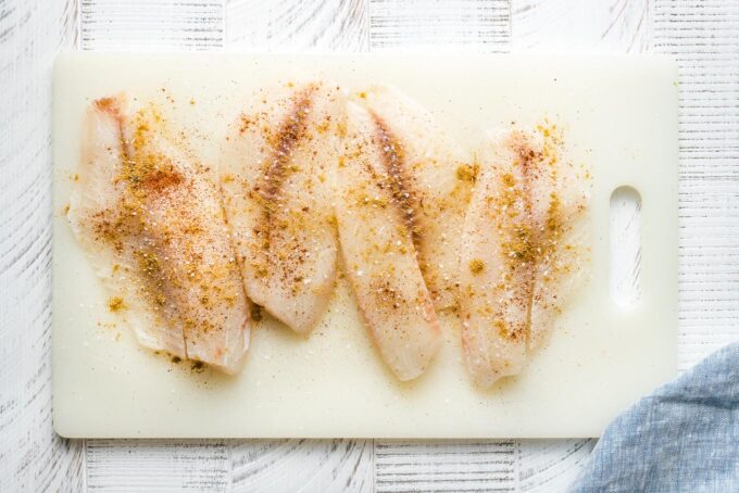 Seasoned tilapia on a cutting board.