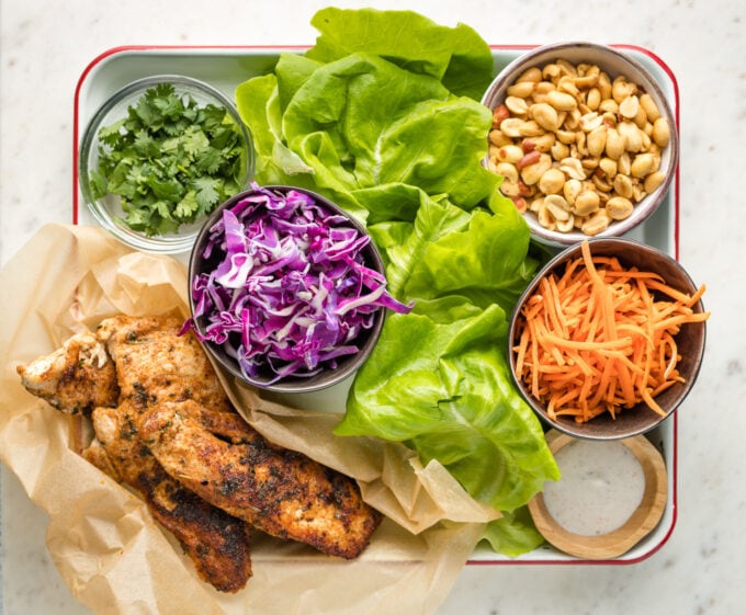 Lettuce, cabbage, jerk chicken, carrots, peanuts, and cilantro laid out in individual prep bowls.