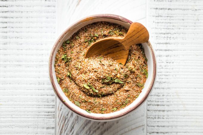 Small bowl with a wooden spoon scooping out Jamaican jerk seasoning.