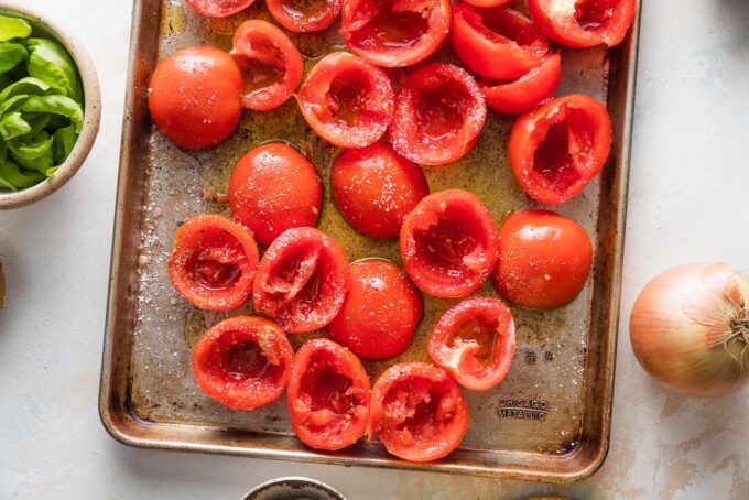 Halved tomatoes with the seeds scraped out arranged on a rimmed baking sheet, ready to roast.