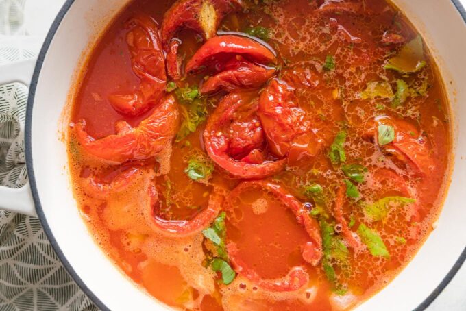 Tomato soup simmering in a large Dutch oven prior to being blended, with visible whole tomatoes and herbs.
