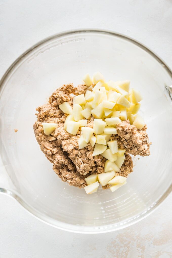 Clear bowl with oatmeal cookie dough and finely chopped apples about to be folded in.