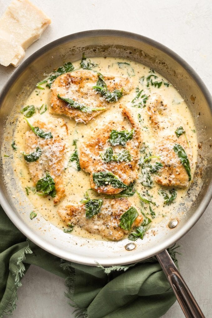 Skillet full of creamy chicken Florentine topped with grated Parmesan cheese.