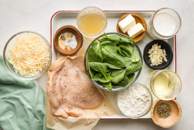 Ingredients arranged on a prep tray - chicken, Parmesan, spinach, flour, butter, garlic, cream, broth, seasonings.