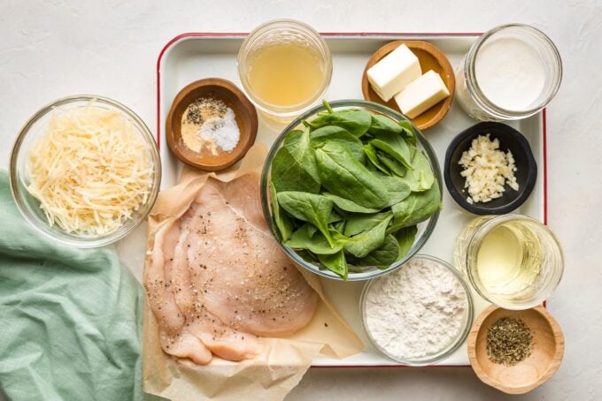 Ingredients arranged on a prep tray - chicken, Parmesan, spinach, flour, butter, garlic, cream, broth, seasonings.
