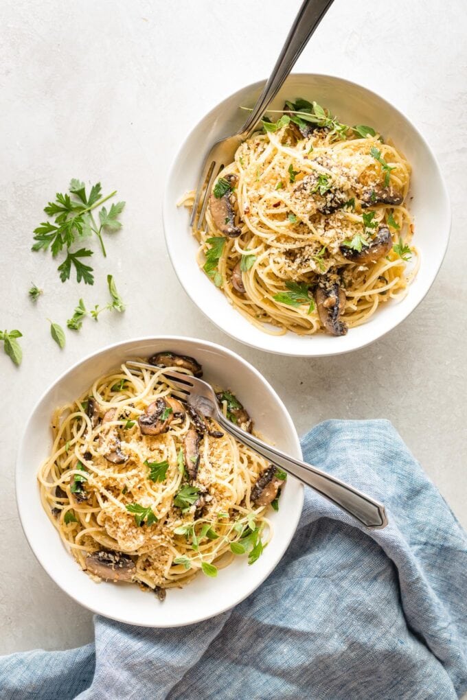 Two bowls of spaghetti with mushrooms, oregano, and toasted breadcrumbs, ready to dig in.
