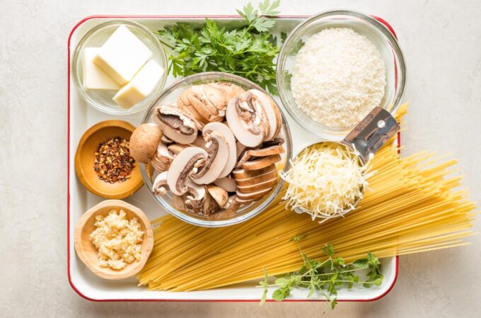 Prep bowls with ingredients: dried spaghetti, mushrooms, breadcrumbs, butter, oregano, parsley, garlic, salt, black pepper, red pepper flakes.