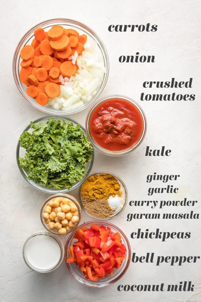 Prep bowls holding ingredients, labeled - "carrots, onion, crushed tomatoes, kale, ginger, garlic, curry powder, garam masala, chickpea, bell pepper, coconut milk.