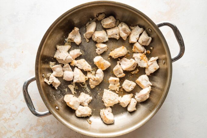 Cubes of chicken cooked in a skillet.