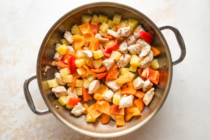 Peppers and pineapple with chicken in the skillet.