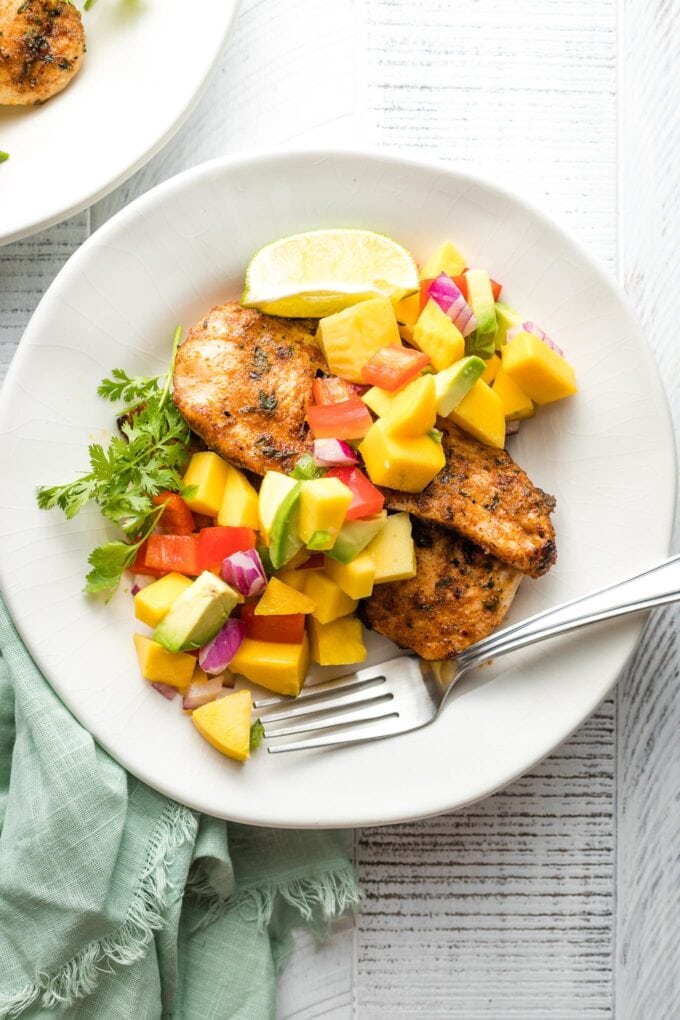 Close up of grilled jerk chicken with mango avocado salsa served on a plate.
