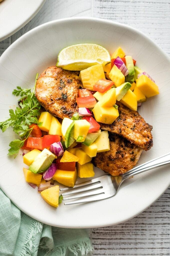 Grilled jerk chicken with mango avocado salsa served on a plate.