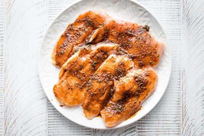 Seasoned raw chicken on a plate.