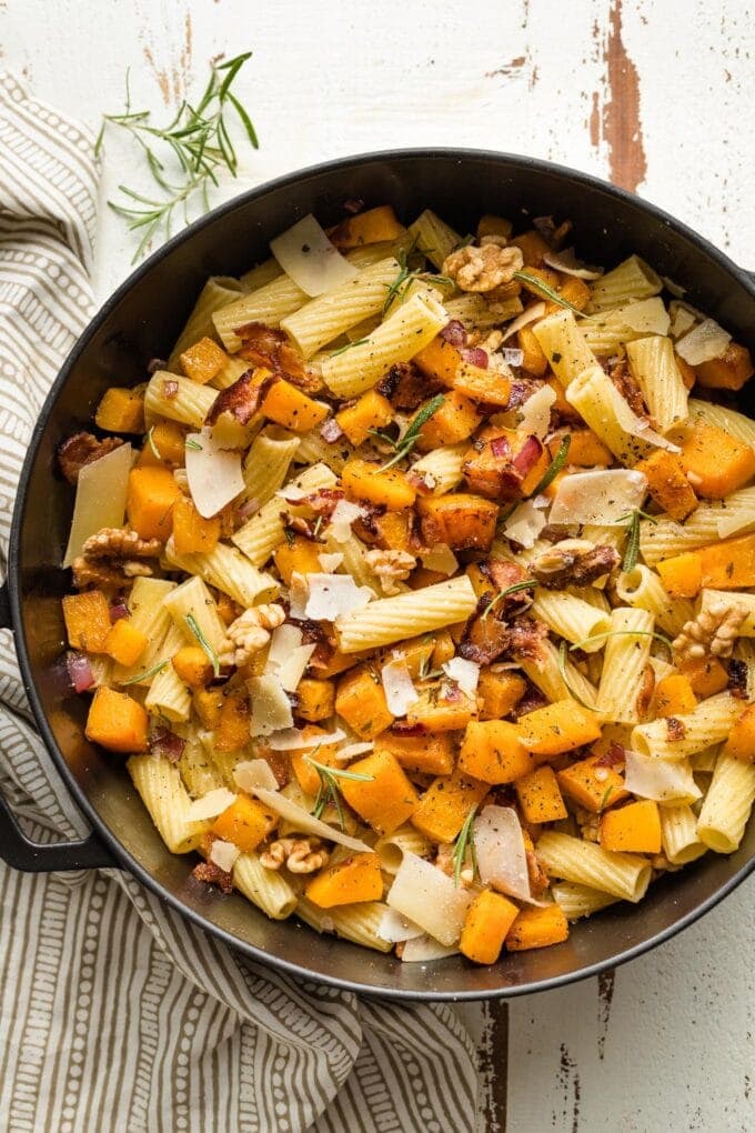 Roasted butternut squash pasta with rosemary and bacon in a skillet.