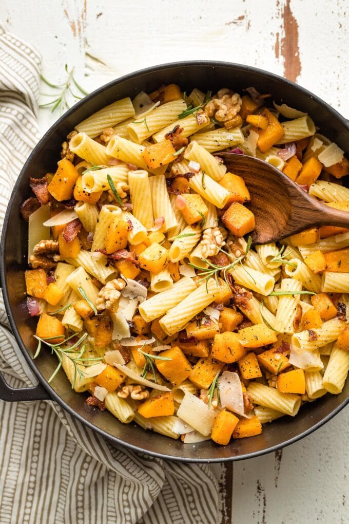 Wooden spoon lifting out servings of pasta from the skillet.