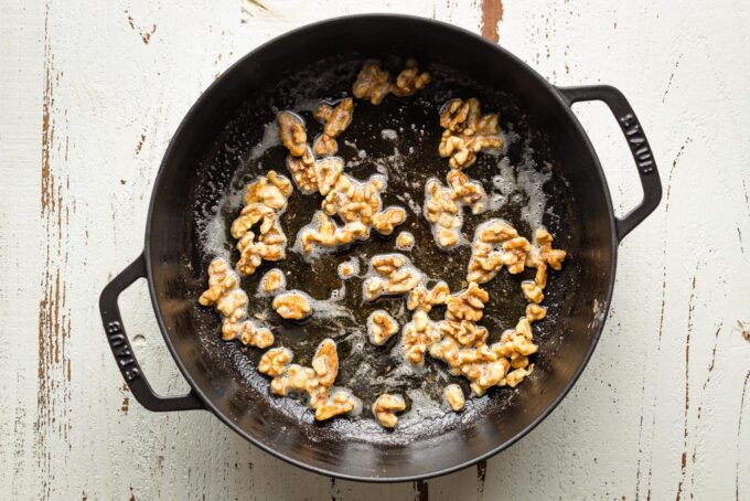 Skillet with toasted walnuts swirled in melted butter and olive oil.