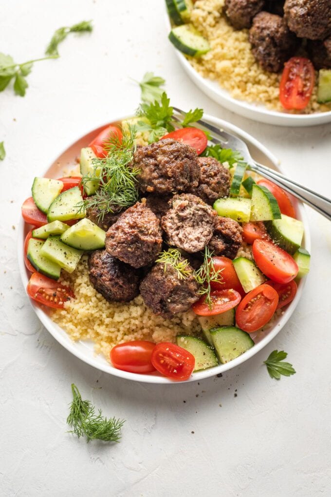 Close-up of lamb meatballs served with couscous and a tomato cucumber salad.