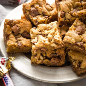 Candy bar blondies on a plate with extra candy wrappers scattered around.