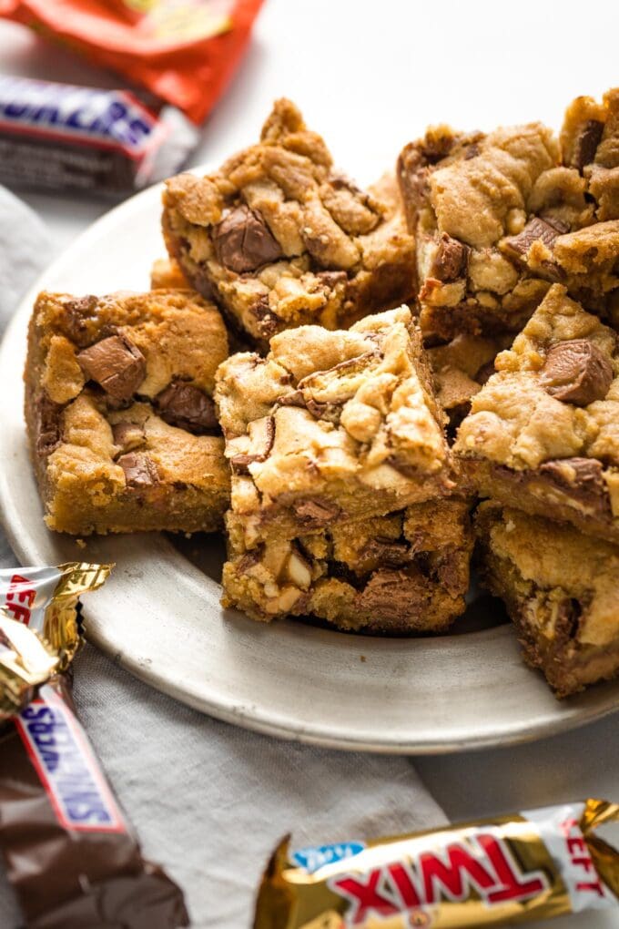 Candy bar blondies on a plate with extra candy wrappers scattered around.