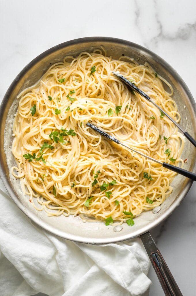 Large skillet filled with creamy garlic butter pasta, with tongs ready to toss the pasta and serve.
