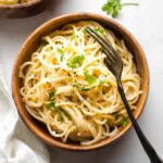 Small bowl of creamy garlic butter pasta with a fork and fresh parsley for garnish.