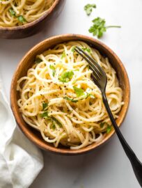 Small bowl of creamy garlic butter pasta with a fork and fresh parsley for garnish.