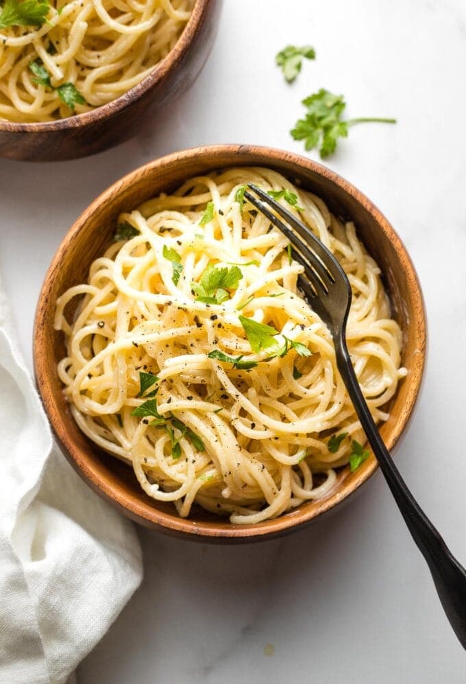 Small wooden bowl with a serving of creamy garlic butter pasta garnished with fresh parsley.