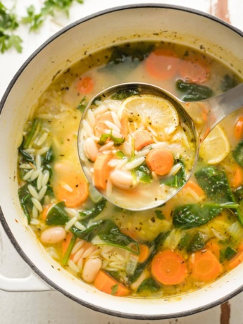 Ladle full of white bean and spinach soup with orzo.