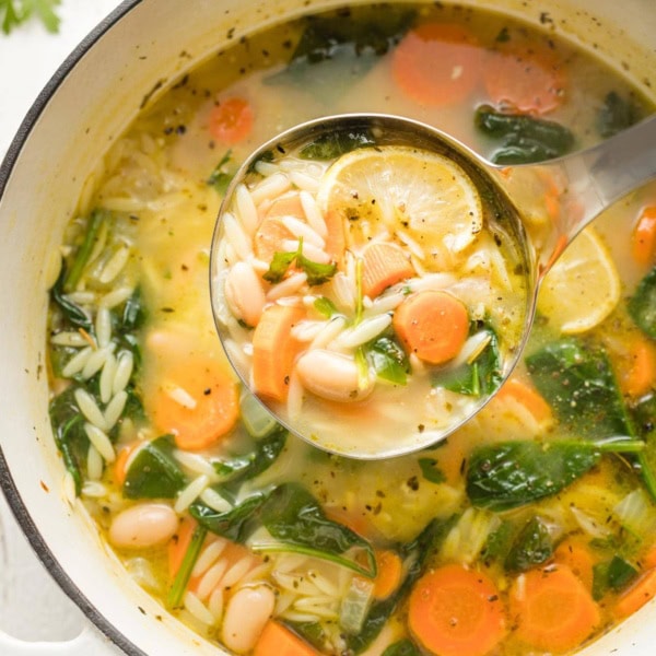 Ladle full of white bean and spinach soup with orzo.