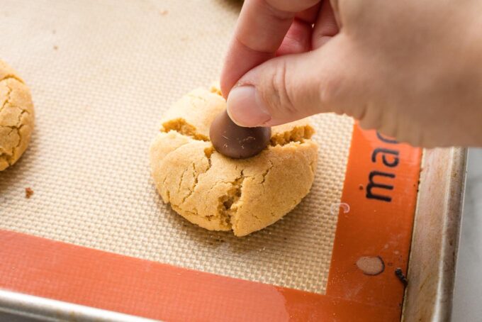 Hand pushing a Hershey's kiss into a just-baked peanut butter cookie to make a peanut butter blossom.