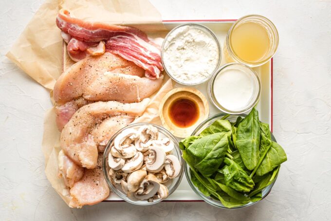 Ingredients - chicken breasts, bacon, flour, broth, mushrooms, spinach, seasonings - laid out on a tray.