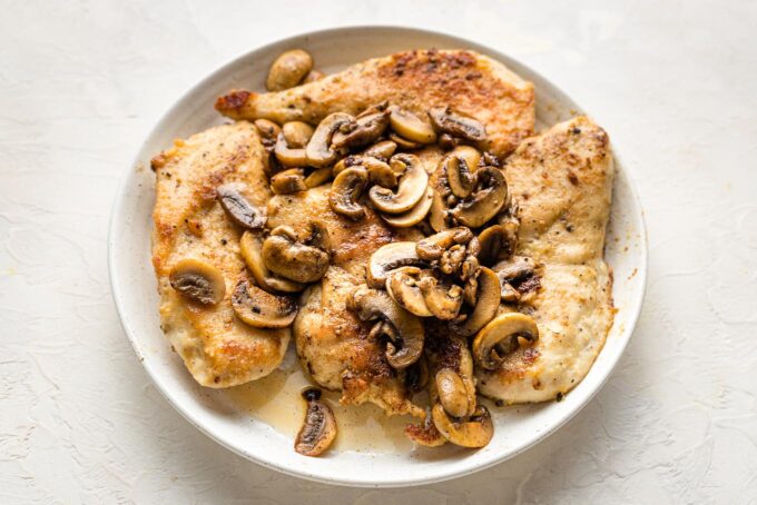 Sauteed chicken and mushrooms set aside on a plate.