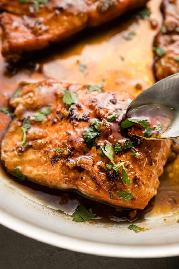 Close-up of a spoon pouring sauce over a salmon filet.