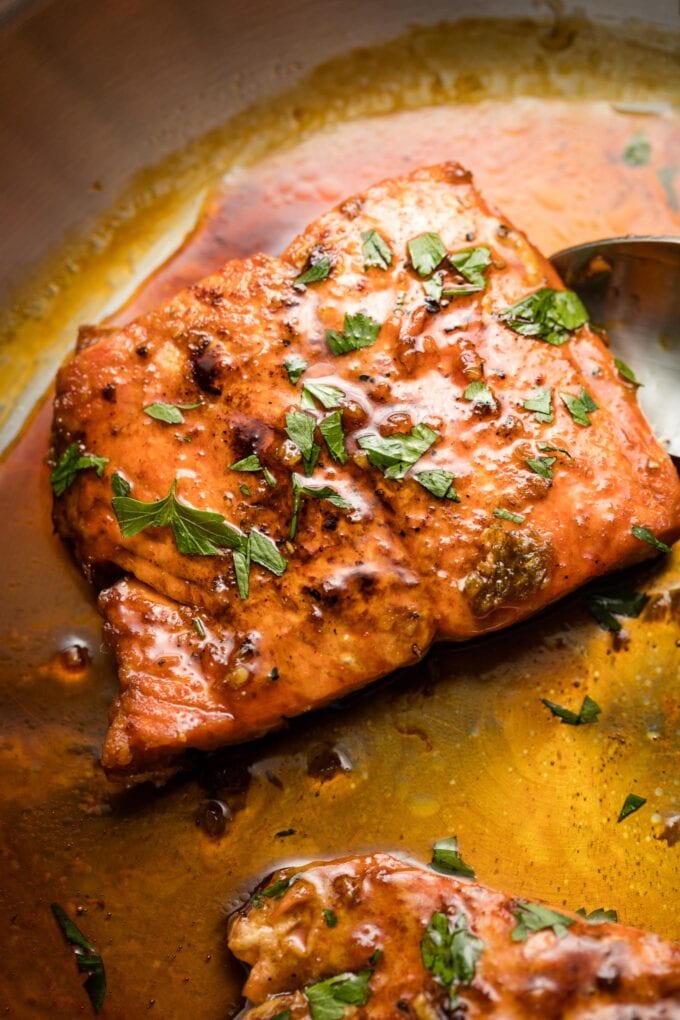 Close up of salmon in pan with honey garlic sauce.