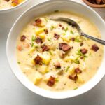 Bowl of potato cheddar chowder garnished with crumbled bacon and chives.