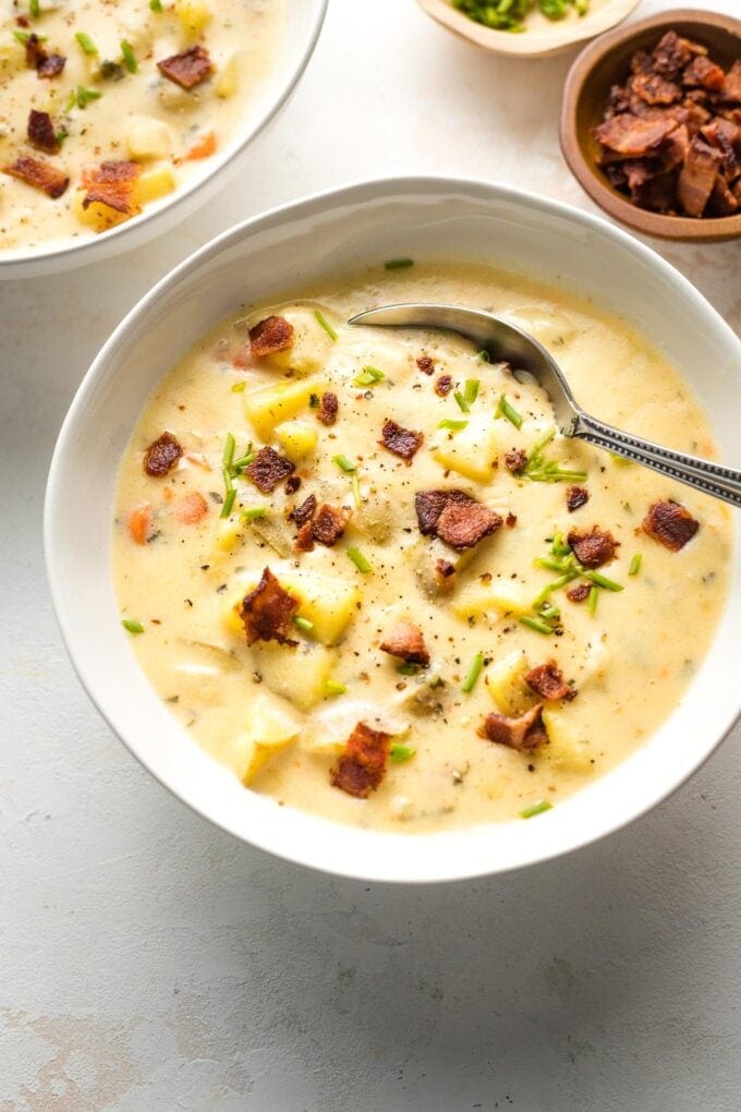 Bowl of potato cheddar chowder garnished with crumbled bacon and chives.