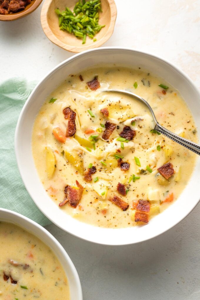 Bowl of potato cheddar chowder garnished with crumbled bacon and chives.