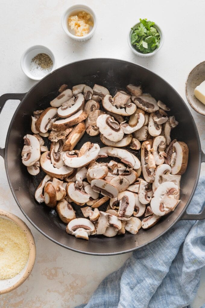 Uncooked mushrooms tossed into a cast iron skillet to saute.