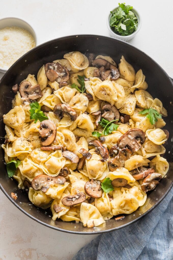 Deep cast iron skillet filled with a dish of cheese tortellini, mushrooms, butter, and Parmesan.