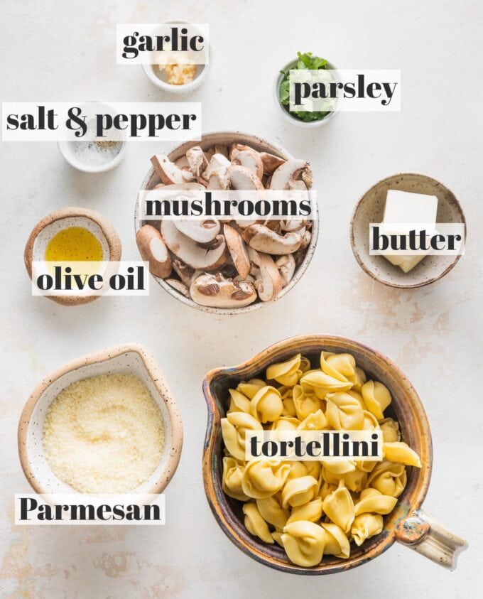 Labeled overhead photo of refrigerated tortellini, sliced mushrooms, butter, Parmesan cheese, garlic, and parsley, all in prep bowls and ready to cook.